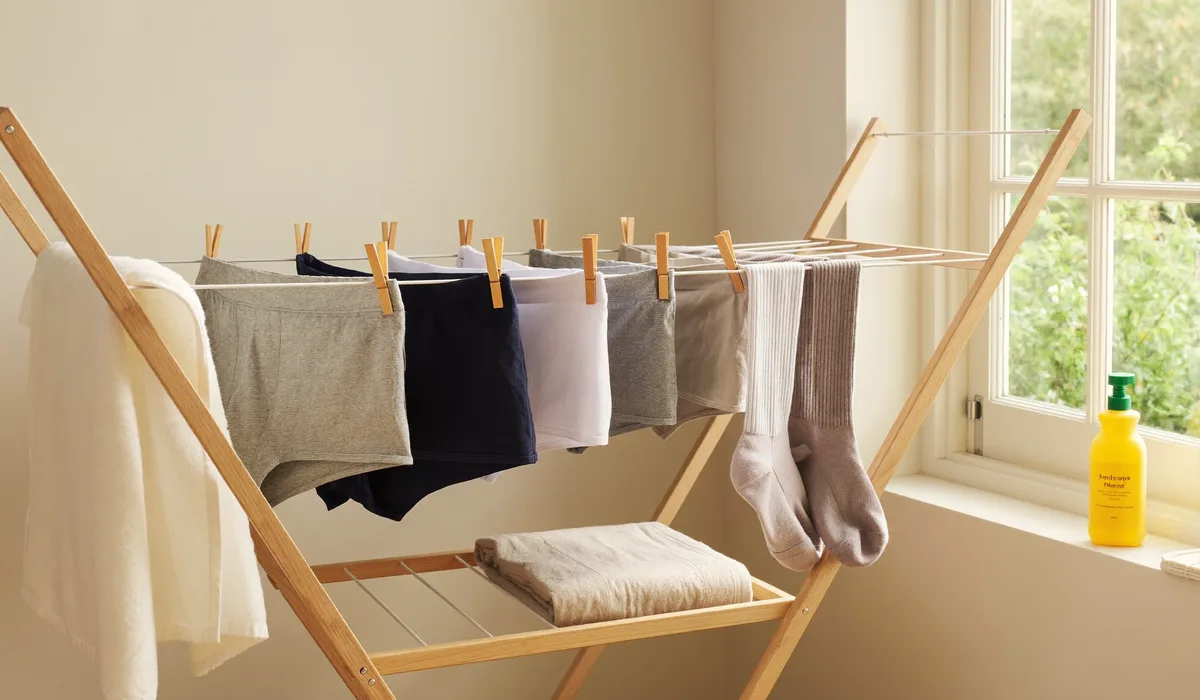 Gewassen boxershorts en sokken hangen te drogen aan een houten droogrek bij het raam